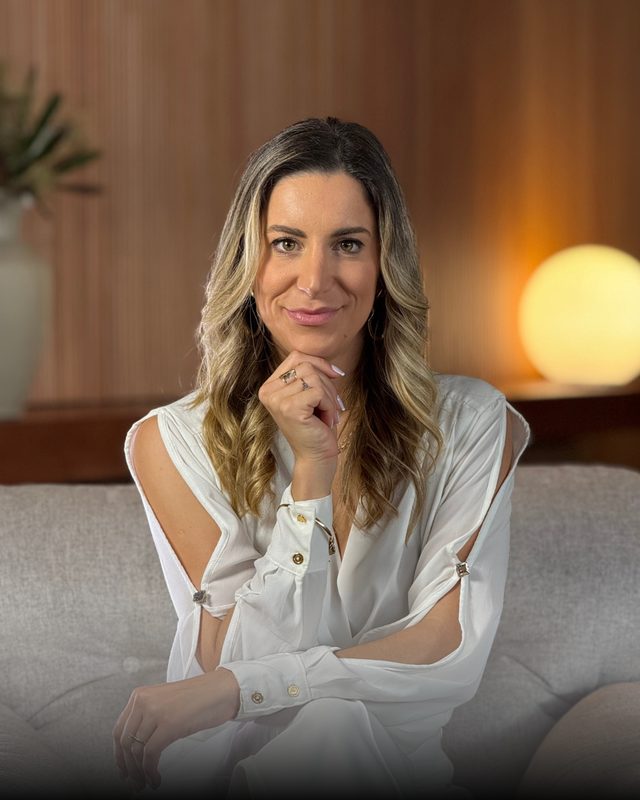 Luísa Crippa sorrindo, de blusa branca, sentada num sofá